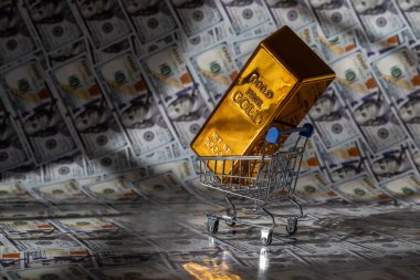 Minyatür bir alışveriş arabasındaki altın külçenin arkasında 100 dolarlık banknotlar var.