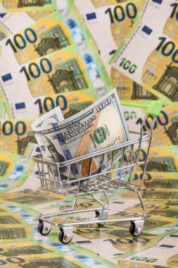 100 dolarlık bir fatura süpermarket alışveriş arabasının arka planında 100 avroluk banknotlarla karşılanıyor.