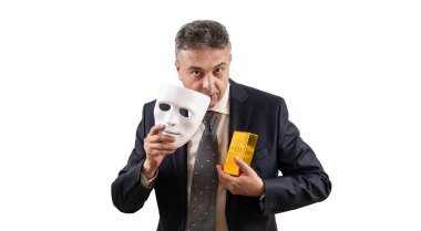 Takım elbiseli orta yaşlı bir adamın elinde beyaz bir maske ve altın külçesi var.