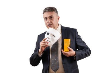 Takım elbiseli orta yaşlı bir adamın elinde beyaz bir maske ve altın külçesi var.