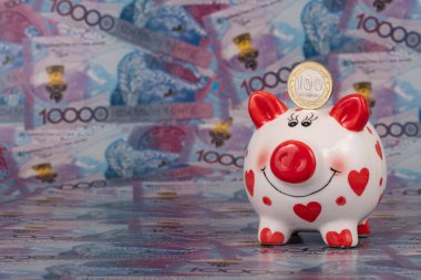 Bir domuz kumbarası ve 100 Kazakistan madeni parasına karşılık 10.000 tenge banknot..