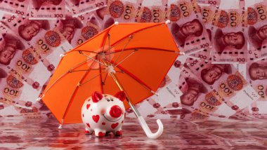 Şemsiyenin altında bir kumbara, arka planda 100 Çin Yuan 'ı var.