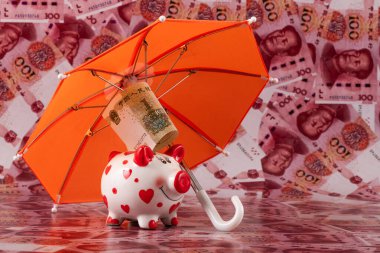 Şemsiyenin altında bir kumbara, arka planda 100 Çin Yuan 'ı var.