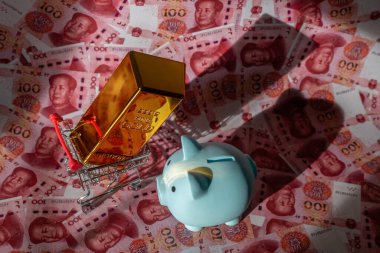 Bir altın külçesi ve bir domuz kumbarası 100 Çin yuan banknotuna karşı.