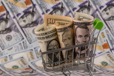 Minyatür bir alışveriş arabasında 1, 5 ve 10 dolarlık banknotlar ve arka planda 100 dolarlık banknotlar.