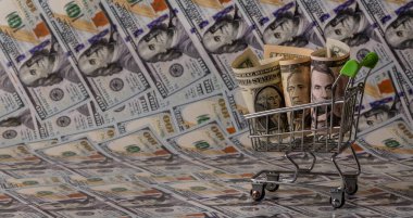Minyatür bir alışveriş arabasında 1, 5 ve 10 dolarlık banknotlar ve arka planda 100 dolarlık banknotlar.