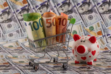 10, 50 ve 100 avroluk banknotlar bir alışveriş arabasında ve bir kumbarada 100 dolarlık banknotlara karşı.