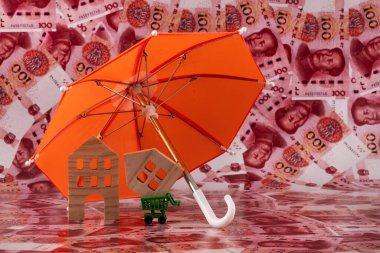 Şemsiyenin altındaki sembolik ahşap evler 100 adet Çin Yuan banknotuna karşı..