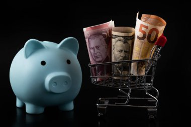 50 Euro, 50 Amerikan doları ve 50 İngiliz sterlini siyah bir arka planda minyatür bir süpermarket alışveriş arabasında.