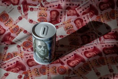 100 $'lık banknotla 100 Yuan' lık banknotları yan yana koyan bir kumbara.