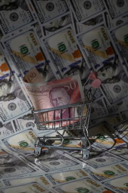 Minyatür bir alışveriş arabasında 50 İngiliz sterlini. Arka planda 100 dolar banknot var.