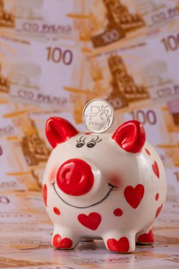 Bir domuz kumbarası ve üzerinde Rus rublesi sembolü olan bir sikke 100 Rus rublesinin arka planına karşı..
