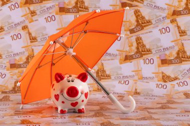 Turuncu bir şemsiyenin altındaki kumbaranın arka planında 100 Rus rublesi var..
