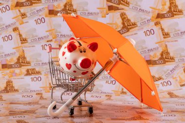 Turuncu bir şemsiyenin altındaki kumbaranın arka planında 100 Rus rublesi var..