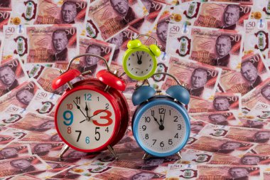 Üç renkli çalar saat İngiliz sterlininin arka planına karşı.