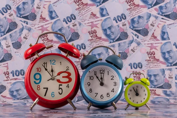 100 Türk lirası 'nın arka planına karşılık üç çalar saat