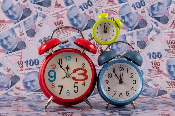 100 Türk lirası 'nın arka planına karşılık üç çalar saat