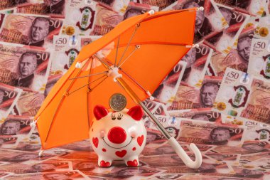 Domuz kumbarası ve şemsiyenin altında İngiliz banknotlarının arka planına karşılık 1 İngiliz sterlini.