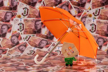 Sembolik bir minyatür ahşap şemsiye altında İngiliz sterlininin arka planına karşı