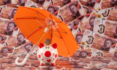 Domuz kumbarası ve şemsiyenin altında İngiliz banknotlarının arka planına karşılık 1 İngiliz sterlini.