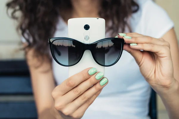 Girl in white t-shirt holding a mobile phone and sunglasses clos