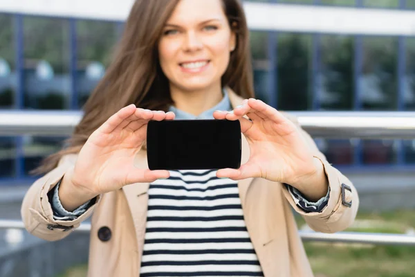 Pretty smiling woman shows the display of the smart phone outdoo