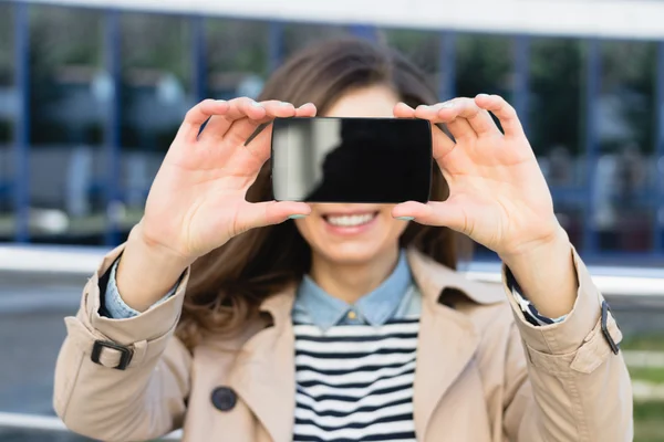 Cute smiling woman shows the display of the smart phone outdoors