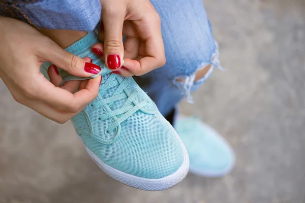 Female hands with a red manicure knotted laces on sports shoes