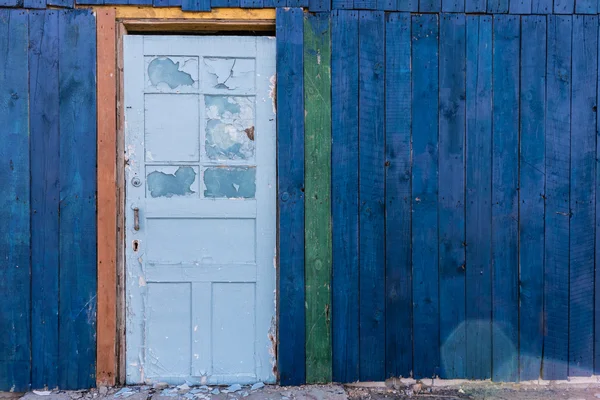 Old wooden light blue door in a dark blue wall