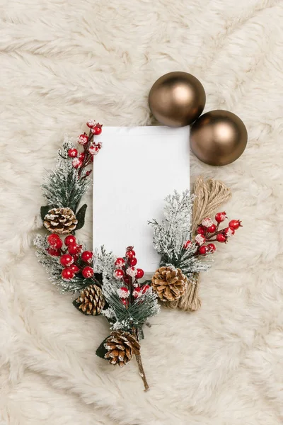 Creative Christmas card layout made of pine branch, baubles, pinecone, red berries with paper card. Flat lay. Nature concept Christmas card with copy space.