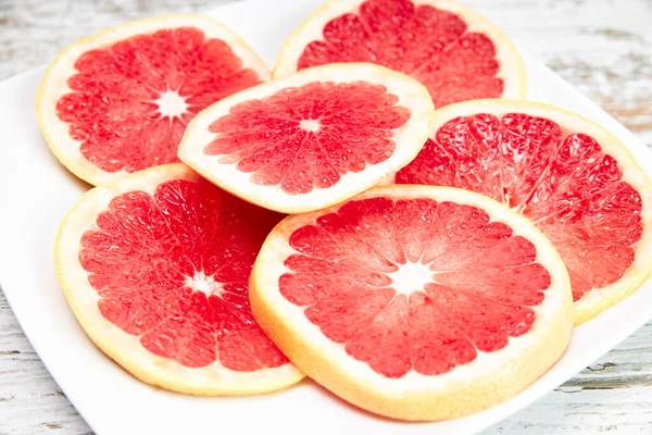 Slices of delicious red grapefruit on a white plate. Concept of healthy fruits.