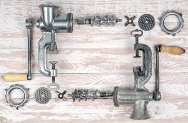 İki eski metal kıyma makinesi ahşap bir kırsal masada parçalanmış..