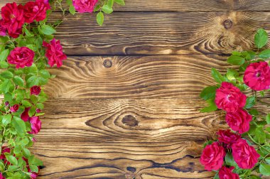 Bir çember şeklinde uzun bir gül ağacı dalı ve yakın plan eski tahtalardan yapılmış ahşap bir masanın arka planında kırmızı çiçek tomurcukları olan bir yarım daire..