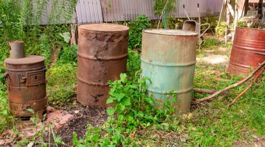 Eski paslı metal fıçıları ve kırsal bir evin arka bahçesinde metal hurdaları yakmak ve çöp öğütücülerini yakmak için bir soba..