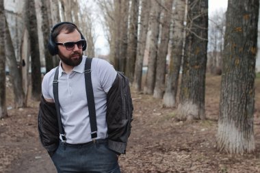 Sakallı ve kulaklıklı bir adam parkta.