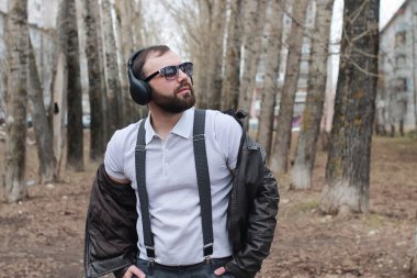 Sakallı ve kulaklıklı bir adam parkta.