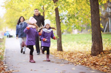 Genç bir aile güneşli bir günde sonbahar parkında yürüyüş yapıyor. Birlikte olmanın mutluluğu..