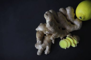 Zencefil kökü bütün ve dilimlenmiş. Koyu arkaplanda limonlu zencefil çayı. Taş zeminde taze zencefil kökü. Vitaminler. Üst Manzara. Metnin için boş yer.