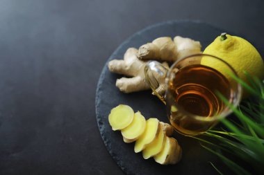Zencefil kökü bütün ve dilimlenmiş. Koyu arkaplanda limonlu zencefil çayı. Taş zeminde taze zencefil kökü. Vitaminler. Üst Manzara. Metnin için boş yer.