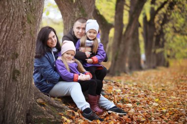 Genç bir aile güneşli bir günde sonbahar parkında yürüyüş yapıyor. Birlikte olmanın mutluluğu..