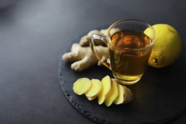 Zencefil kökü bütün ve dilimlenmiş. Koyu arkaplanda limonlu zencefil çayı. Taş zeminde taze zencefil kökü. Vitaminler. Üst Manzara. Metnin için boş yer.