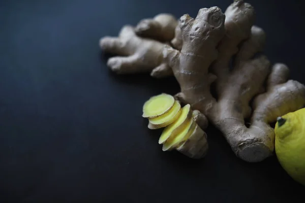 Ginger root whole and sliced. Ginger tea with lemon on the dark background. Fresh ginger root on stone background. Vitamins. Top view. Free space for your text.