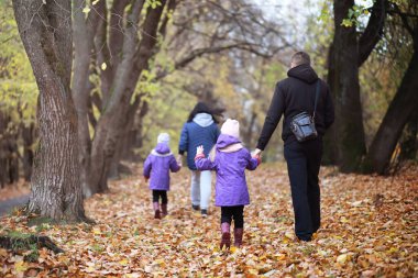 Genç bir aile güneşli bir günde sonbahar parkında yürüyüş yapıyor. Birlikte olmanın mutluluğu..