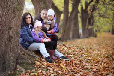 Genç bir aile güneşli bir günde sonbahar parkında yürüyüş yapıyor. Birlikte olmanın mutluluğu..