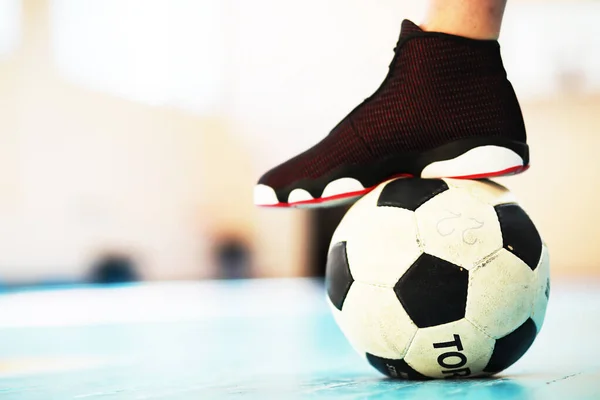 A human foot rest on the football on concrete floor. Photo of one soccer ball and sneakers in a wooden floor