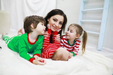 Çizgili pijamalı bir aile evde dinleniyor. Elf gibi giyinmiş küçük çocuklar kanepede yatıyor. Mutlu bir aile..