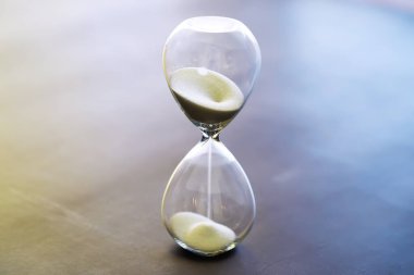 Kum saati ampulleri arasında koşan ve bir geri sayım bitiş tarihine kadar geçen zamanı ölçen, fotokopi alanı olan karanlık bir zemin arka planında..