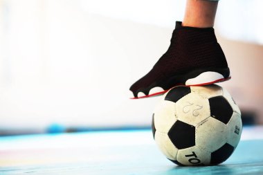 Beton zeminde bir insan ayağı dinleniyor. Ahşap zeminde bir futbol topu ve spor ayakkabısının fotoğrafı.