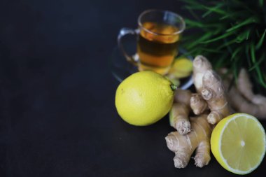 Zencefil kökü bütün ve dilimlenmiş. Koyu arkaplanda limonlu zencefil çayı. Taş zeminde taze zencefil kökü. Vitaminler. Üst Manzara. Metnin için boş yer.