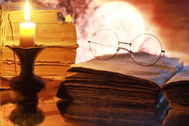 Ay 'ın arka planında eski bir retro kitapta antika gözlükler. Mum ışığından kitap okuyor. Kitap gerilim ve roman konsepti..